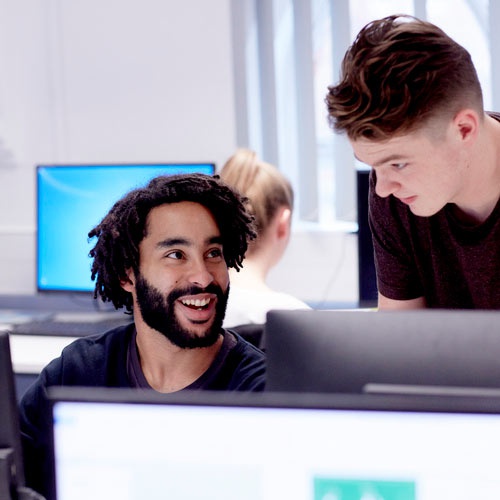 Two students chat while working at a computer. 