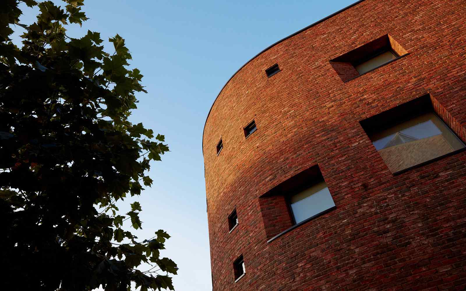 A brick building with curved wall in front of a blue sky. 