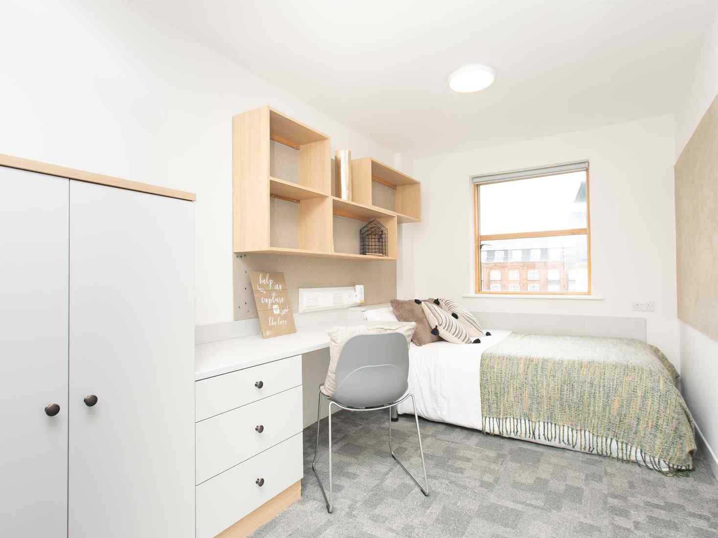 Classic ensuite plus room at Abode accommodation site, with wardrobe, desk and drawers, bed, chair, and wall shelving. 