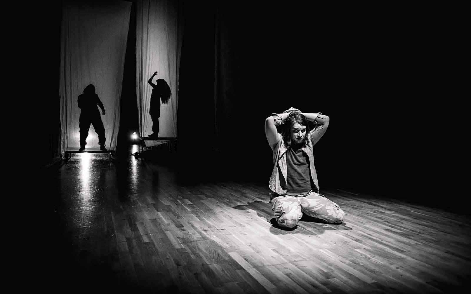 Black and white image of student acting, on floor with arms over head 