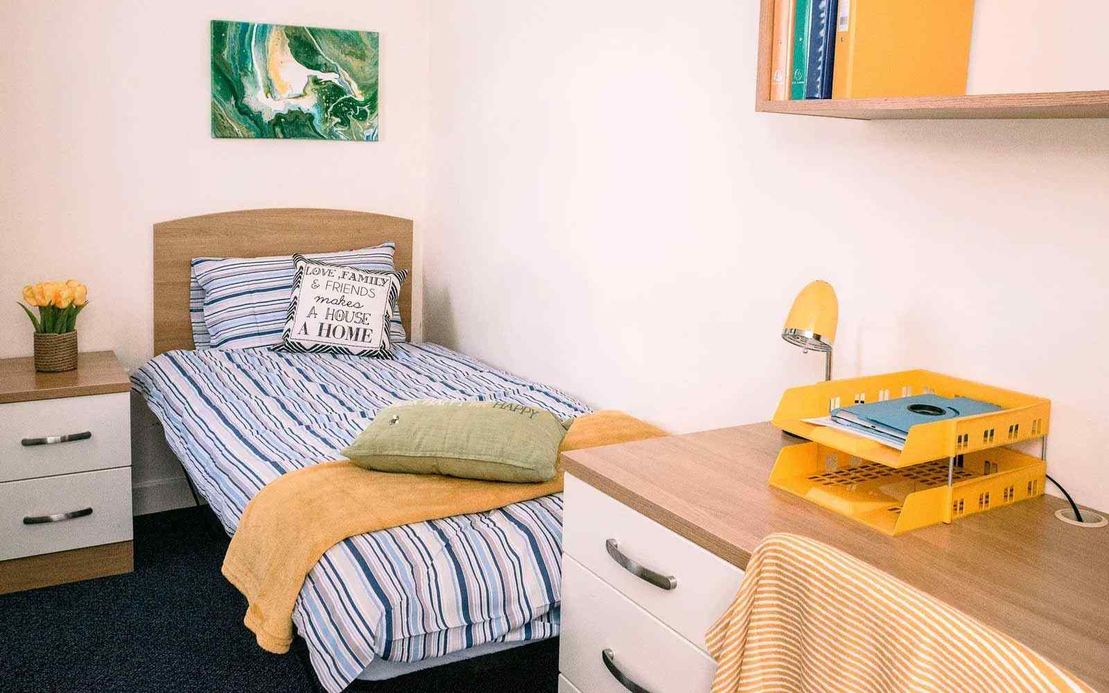 View of a room in Garden Street accommodation with bed, cushions, desk, shelves and wall art. 