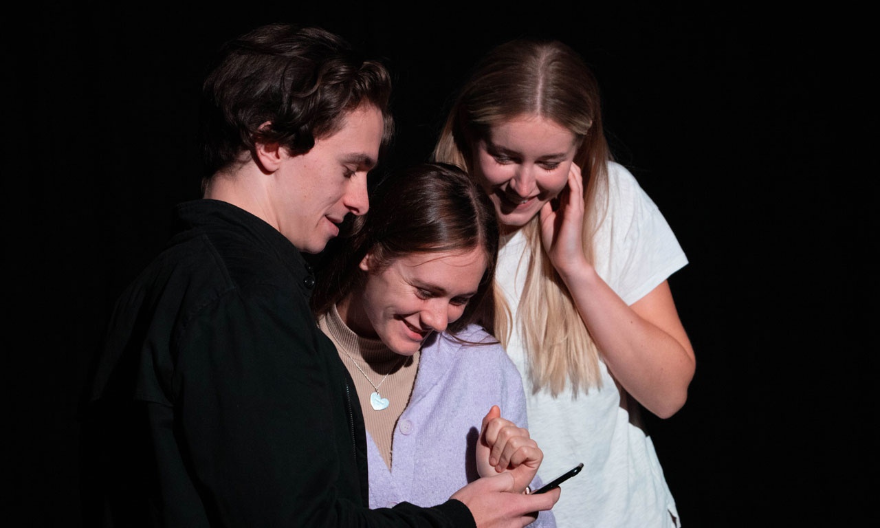 Three actors on stage, looking at phone screen and smiling 