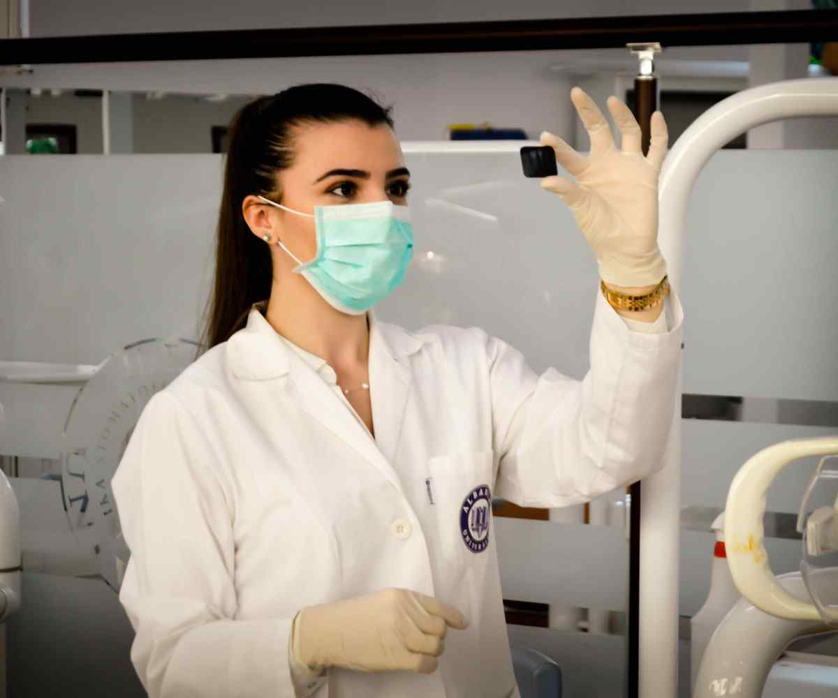 Woman in lab coat, gloves and face mask looking at slide 