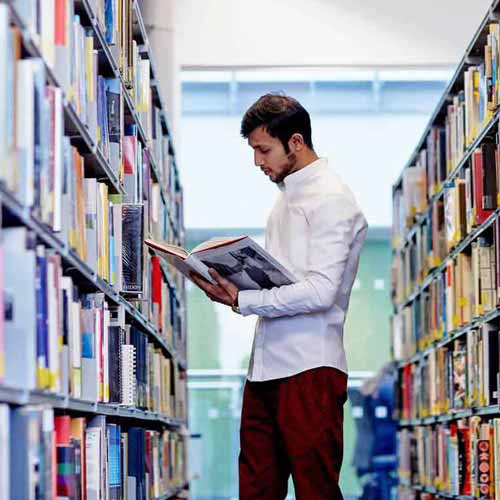 Student looking at book next to library shelves 