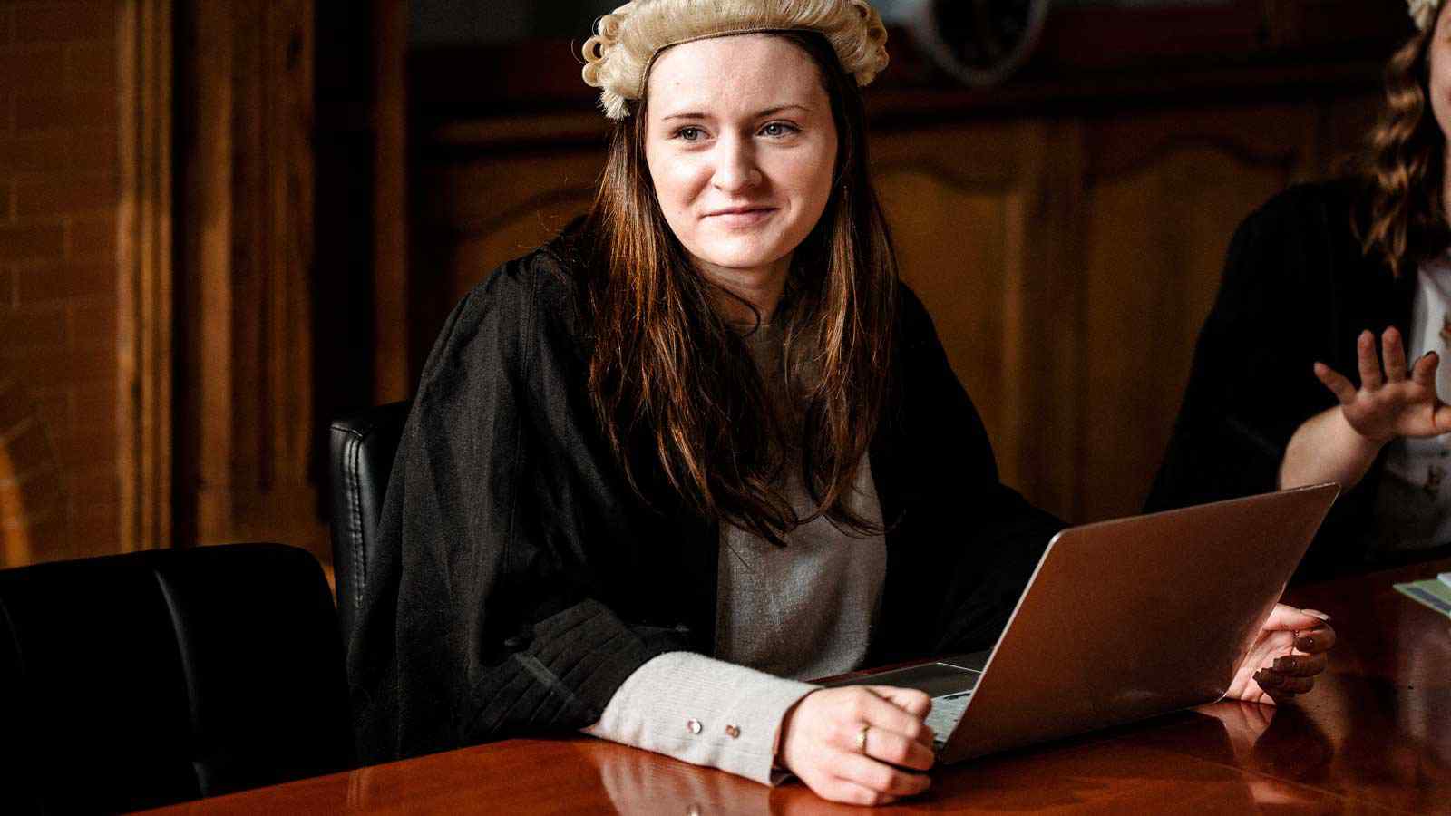Law student wearing barrister wig sitting at table with laptop in courtroom 