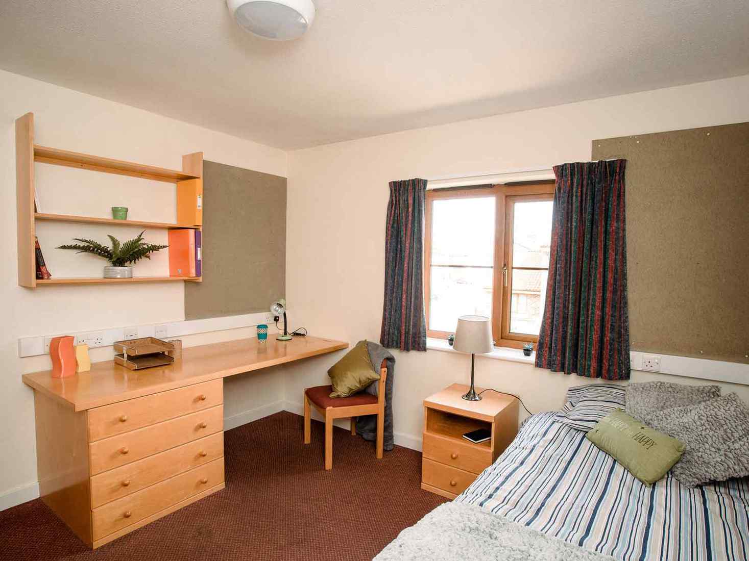 Student bedroom in Limes Court with bed, desk, side table, shelves and noticeboard 