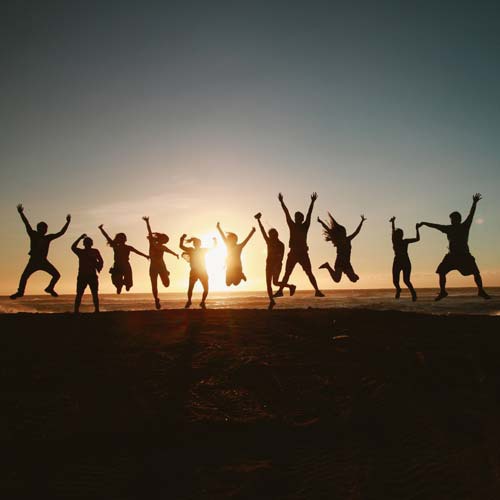 Silhouettes of line of figures jumping in celebration in front of sunset 