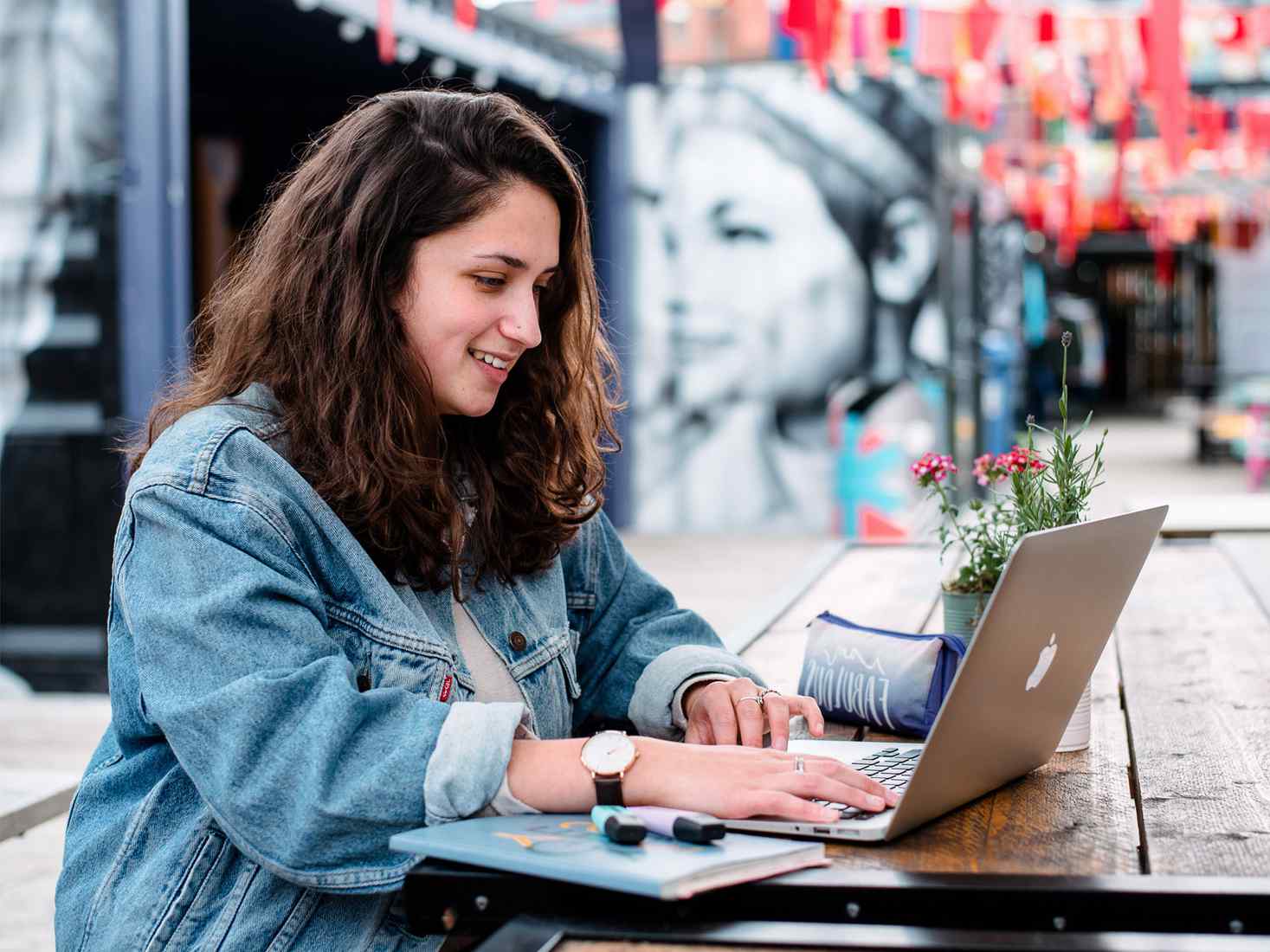 Female student, working on a laptop, in front of a mural at Spark York  