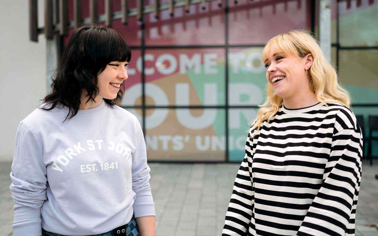Two members of Students' Union team smiling in conversation outside SU building 
