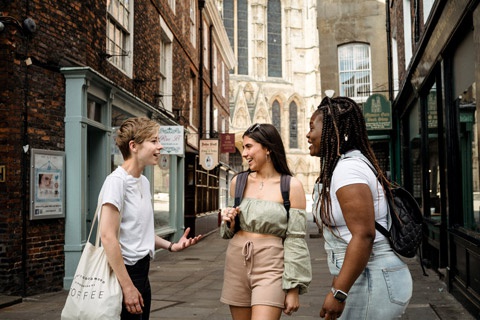 Three students chatting in street of York with Minster in background 
