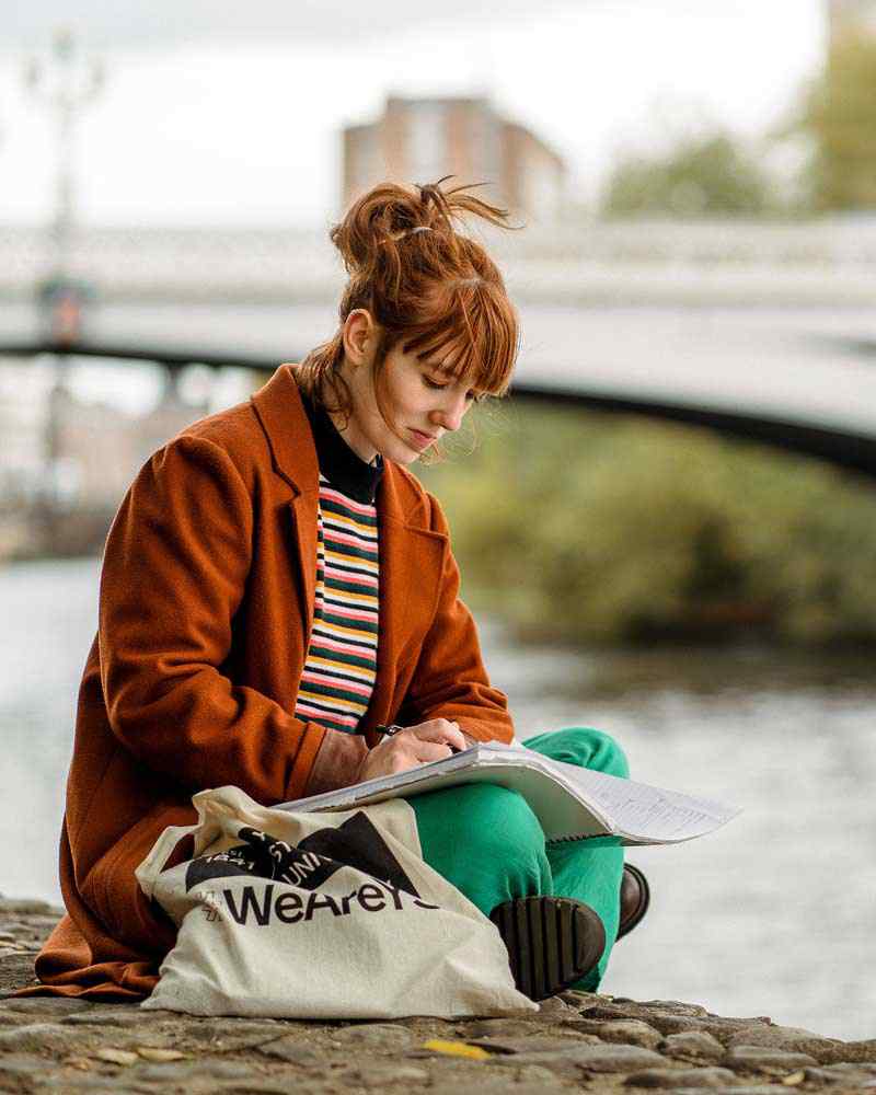 A student sits and works next to the river in York. 