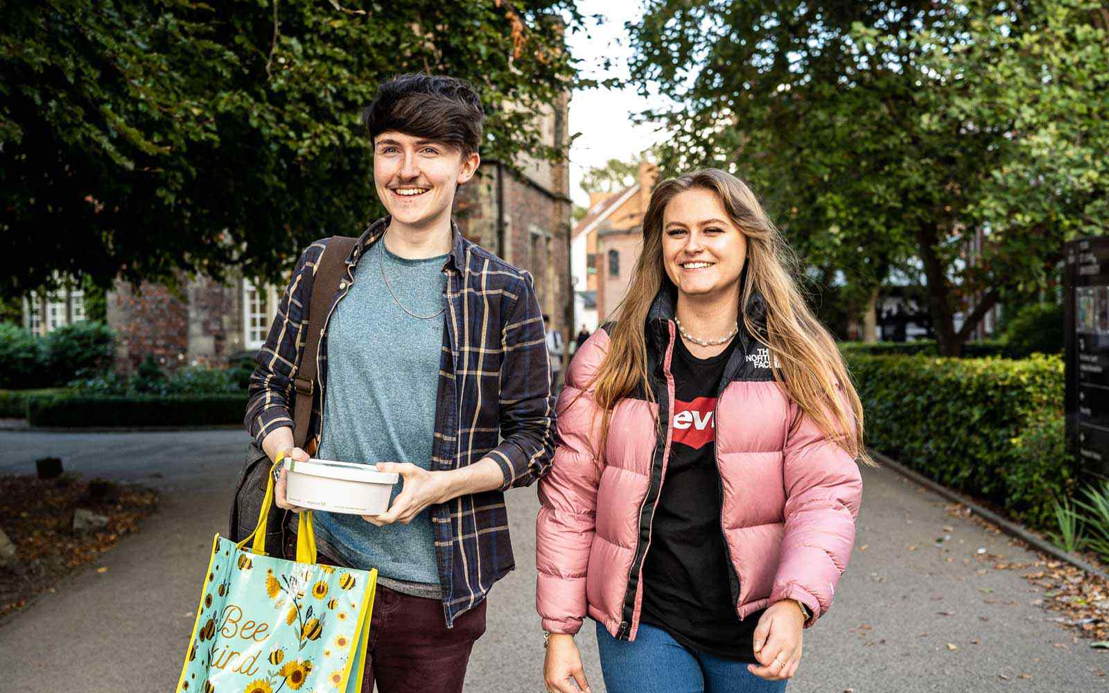 Two smiling students walk onto campus 