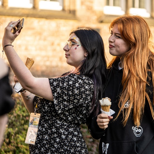 Two students wearing face paint and holding ice creams posing for selfie 