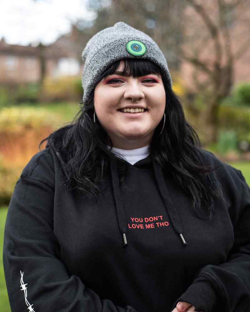 A student in a hoody and hat smiles at the camera 
