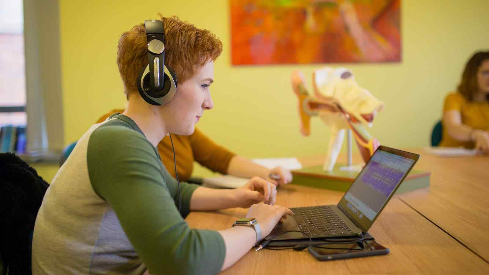 A language student works on a laptop with headphones. 