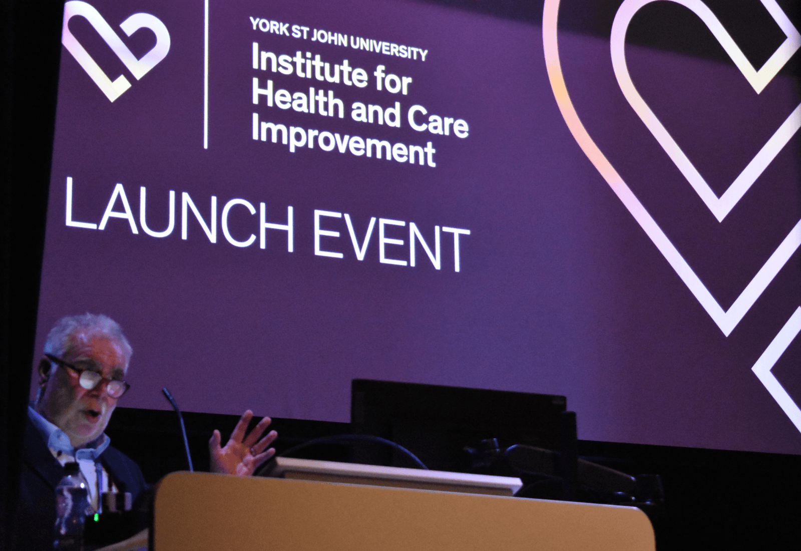 A man speaking at a lecturn in front of a launch event banner 